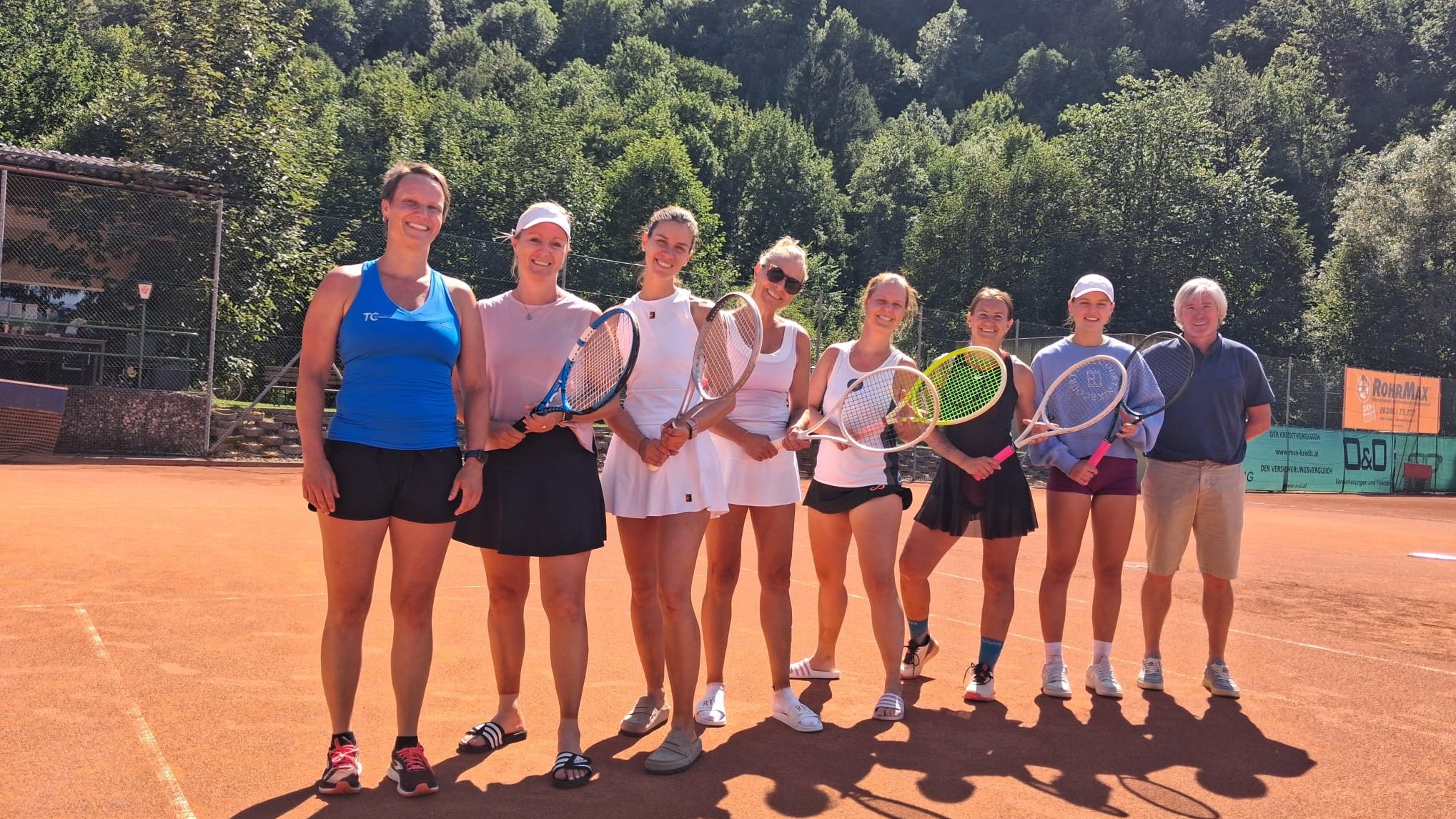 Tennis-Damen mit Schlägern in Österreich vor Bäumen und Werbung